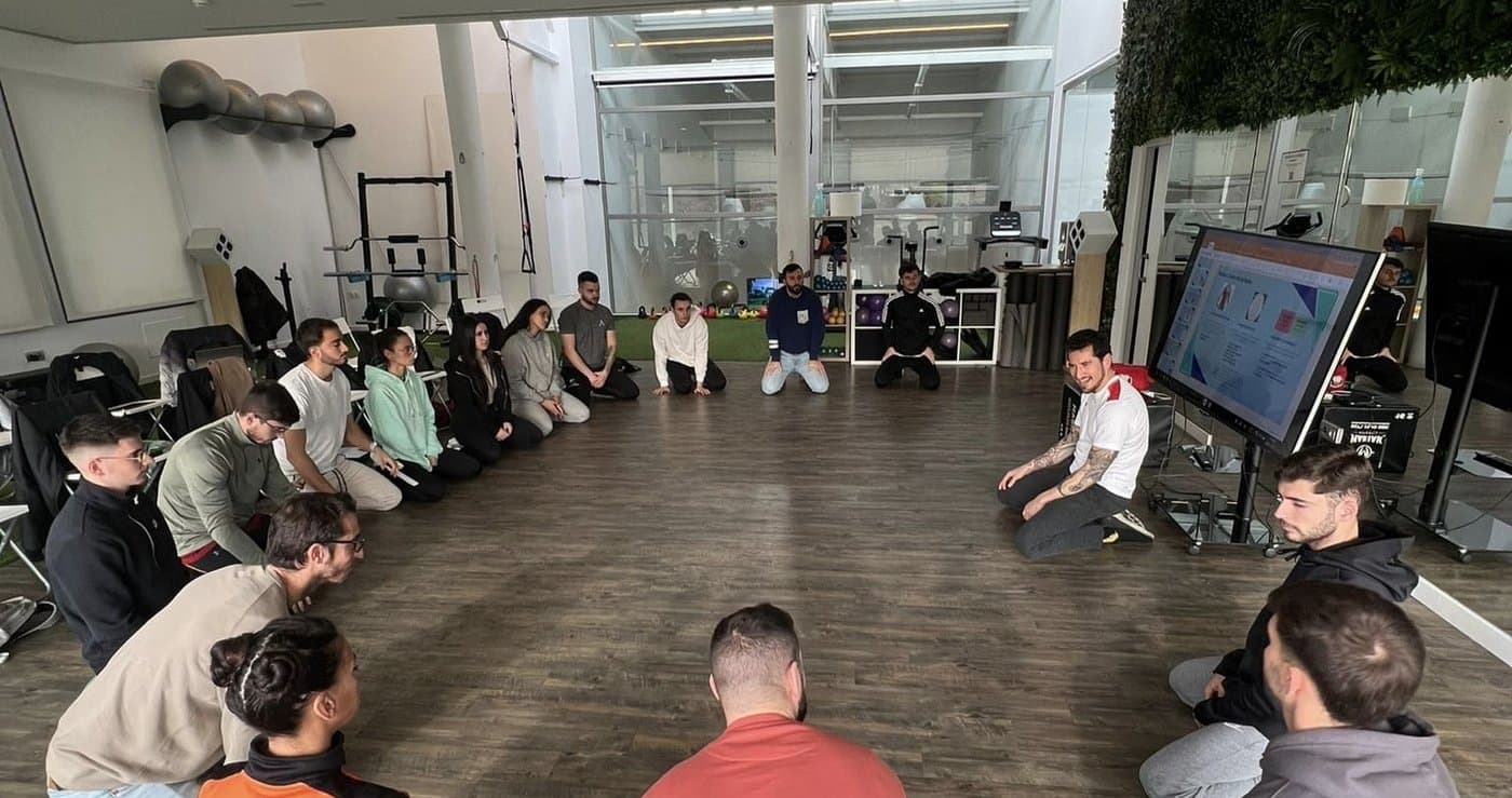 Turma sentada em círculo numa sala de treino, em sessão prática com Alejandro Molinero